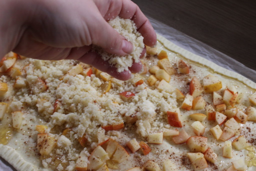Aus einigen Zutaten werden Brösel hergestellt und über den Blätterteig Kuchen verteilt.