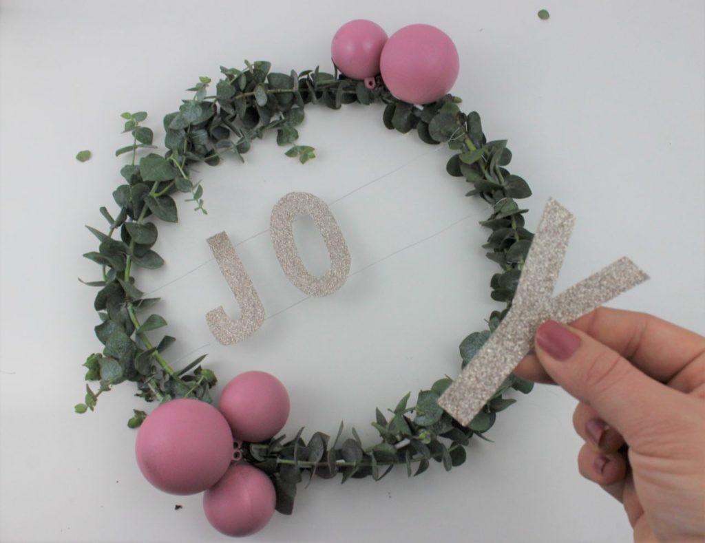 Das weihnachtliche Wort wird in der Mitte des Türkranzes befestigt.