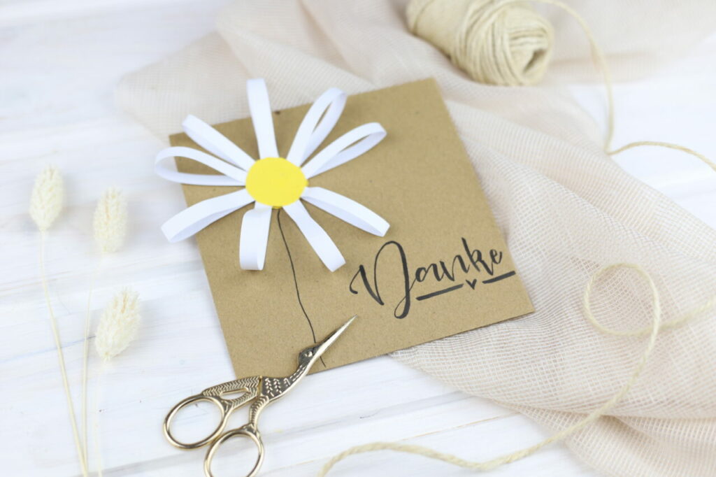 Die Papierblume wird auf eine Karte geklebt und dient nun als Grußkarte oder Karte zum Geburtstag oder Muttertag.